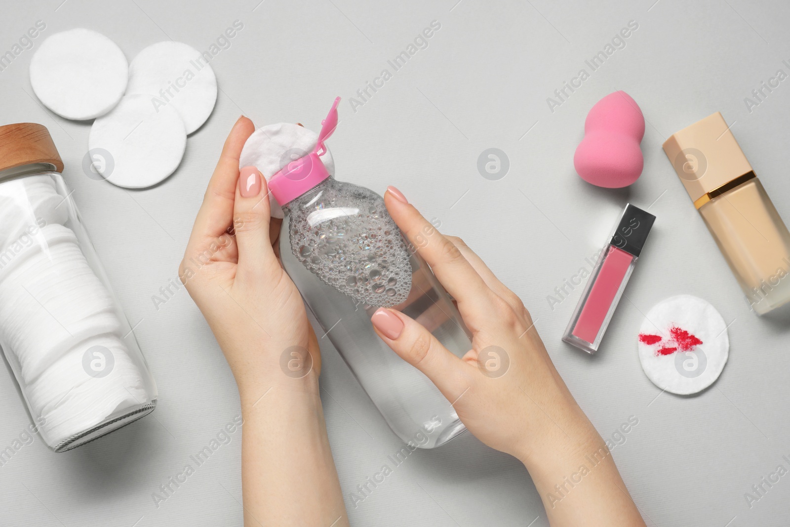 Photo of Woman using makeup remover, closeup. Cotton pads, lip gloss, foundation and sponge on light grey background, top view