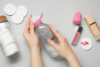 Woman using makeup remover, closeup. Cotton pads, lip gloss, foundation and sponge on light grey background, top view