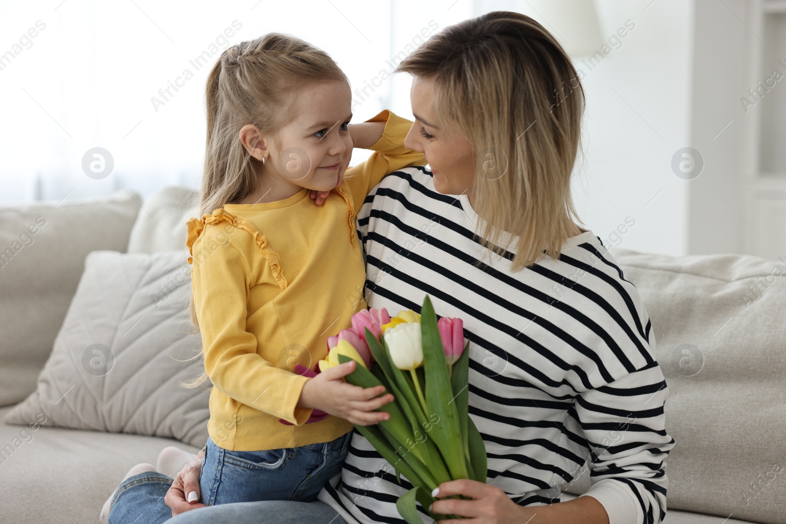 Photo of Little daughter congratulating her mom with Mother`s Day at home. Woman holding bouquet of beautiful tulips