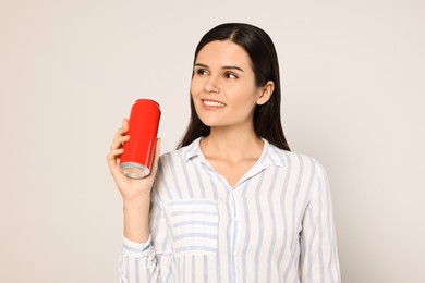 Beautiful young woman holding tin can with beverage on light grey background