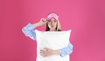 Young woman with pillow and sleep mask on pink background