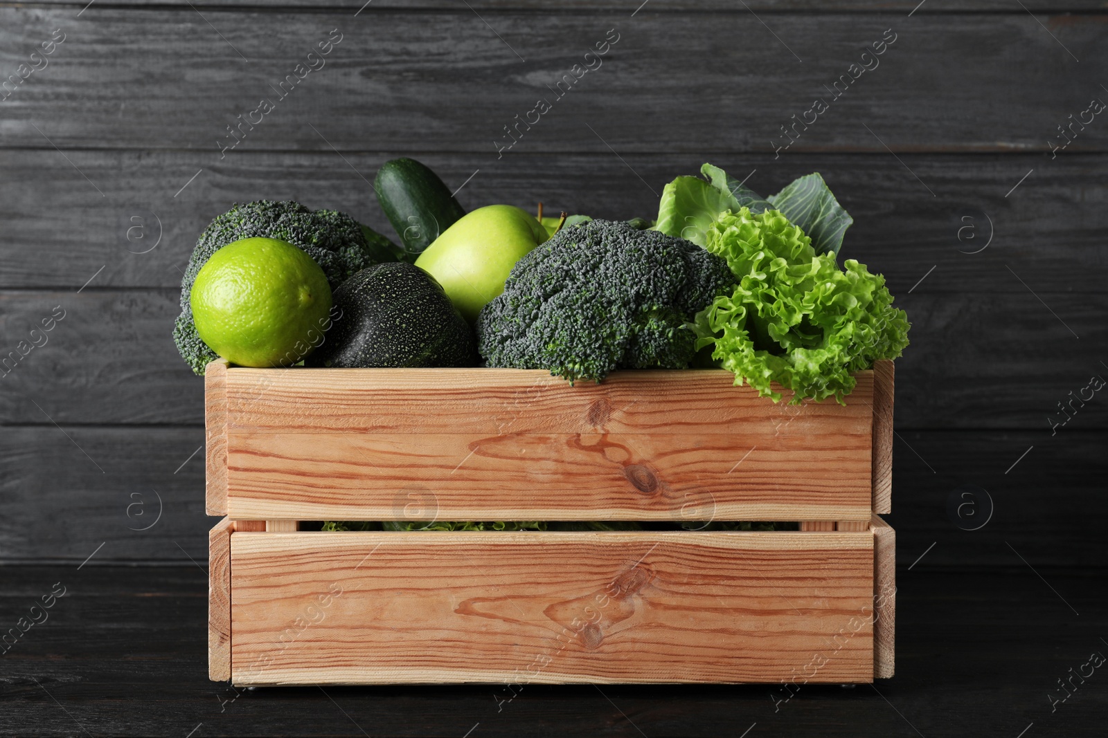 Photo of Wooden crate full of fresh green fruits and vegetables on dark background