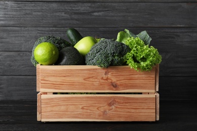 Photo of Wooden crate full of fresh green fruits and vegetables on dark background