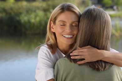 Family portrait of mother and daughter hugging near pond. Space for text