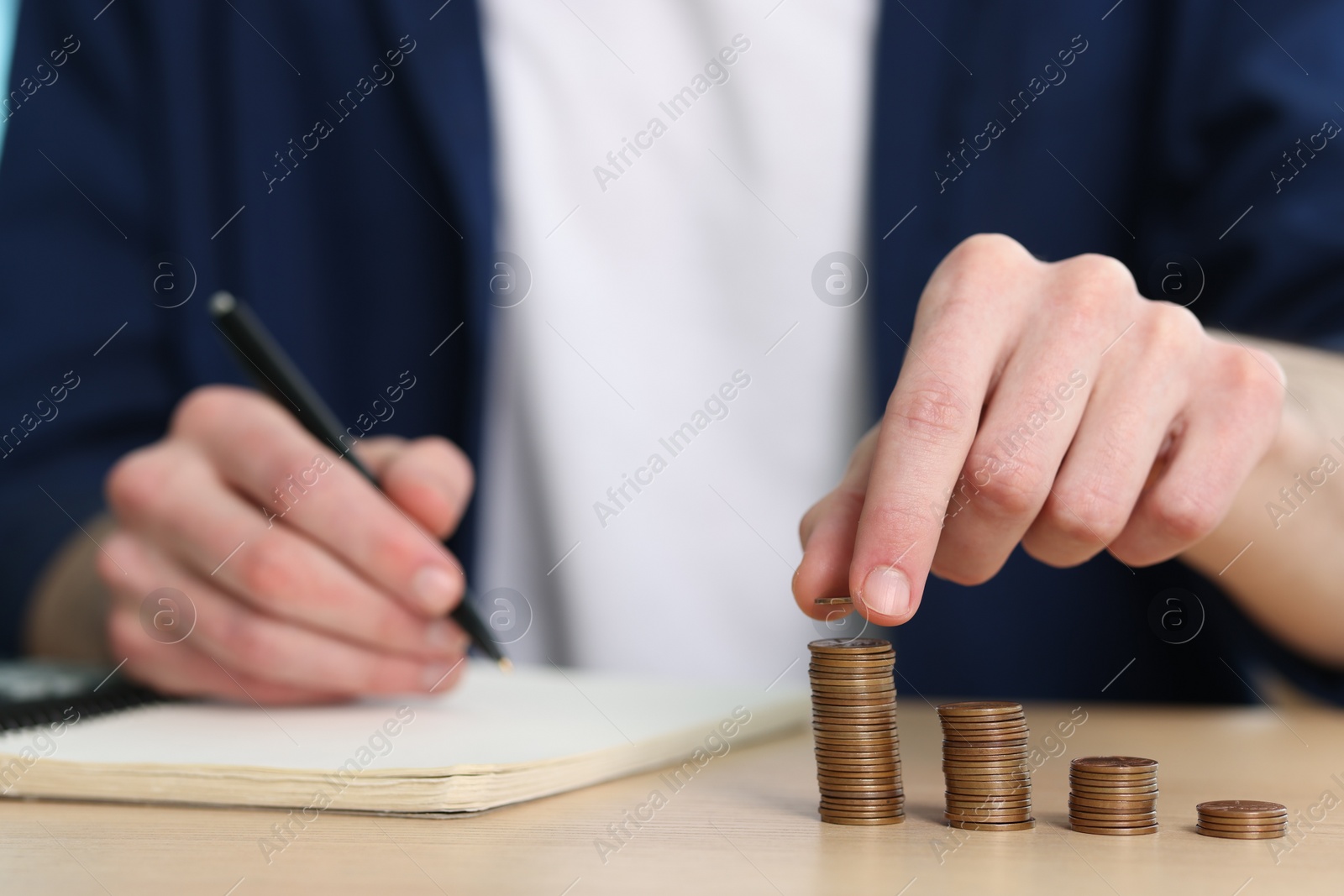 Photo of Financial savings. Man stacking coins at wooden table, closeup