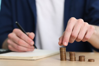 Photo of Financial savings. Man stacking coins at wooden table, closeup