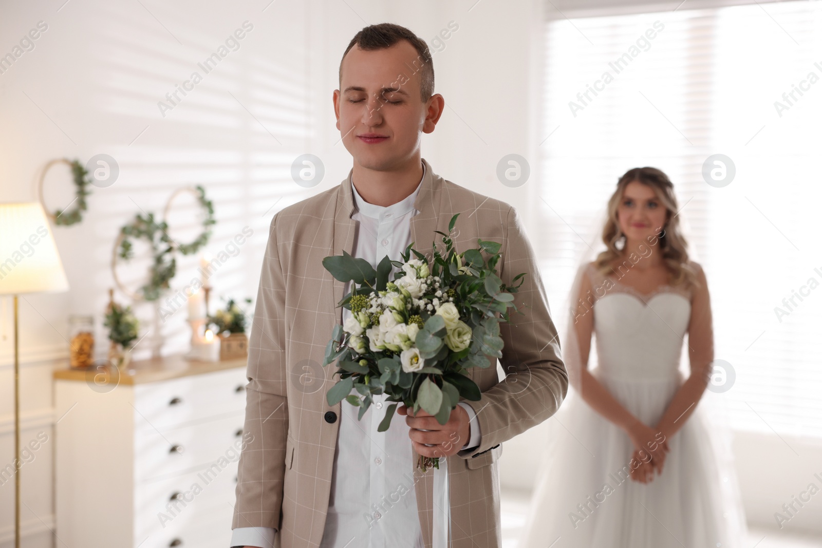 Photo of Groom with closed eyes waiting for his lovely bride indoors. First meeting at wedding day