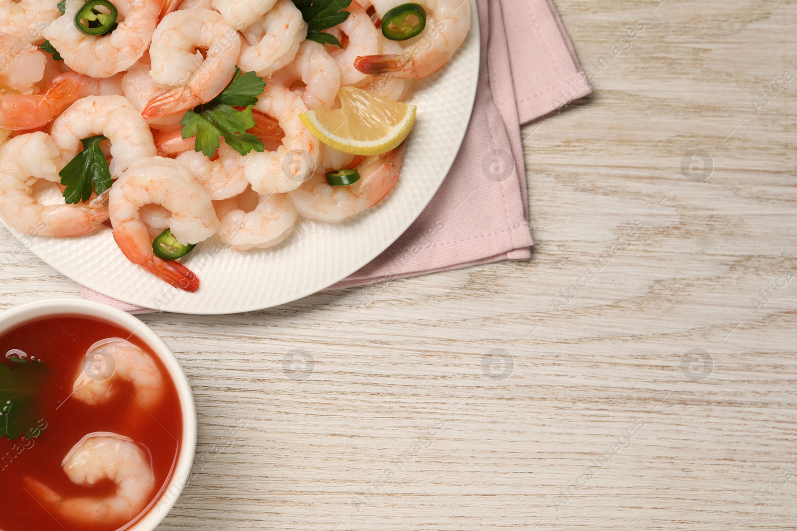 Photo of Tasty boiled shrimps with cocktail sauce, chili, parsley and lemon on light wooden table, flat lay. Space for text