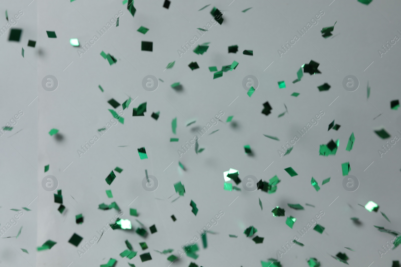 Photo of Shiny green confetti falling down on light grey background