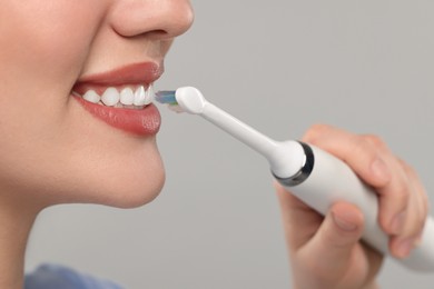Photo of Woman brushing her teeth with electric toothbrush on light grey background, closeup