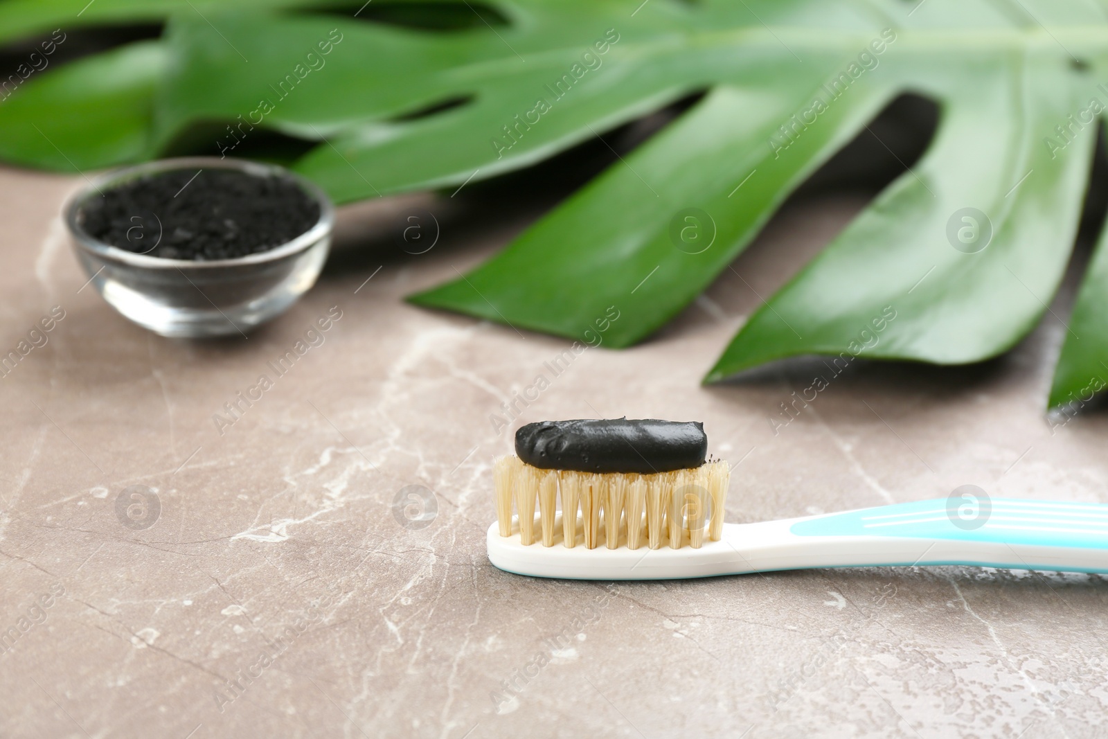 Photo of Toothbrush with natural bristles and charcoal paste on grey marble table, closeup. Space for text