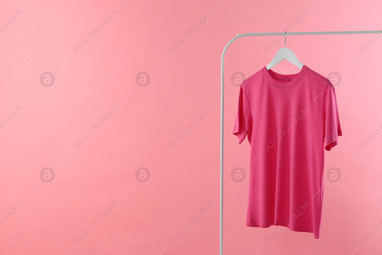 Photo of Rack with stylish t-shirt on pink background. Space for text
