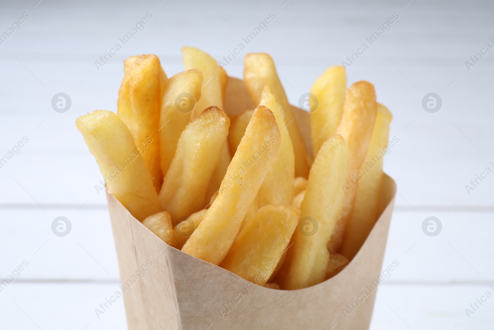 Photo of Delicious french fries in paper box on light background, closeup