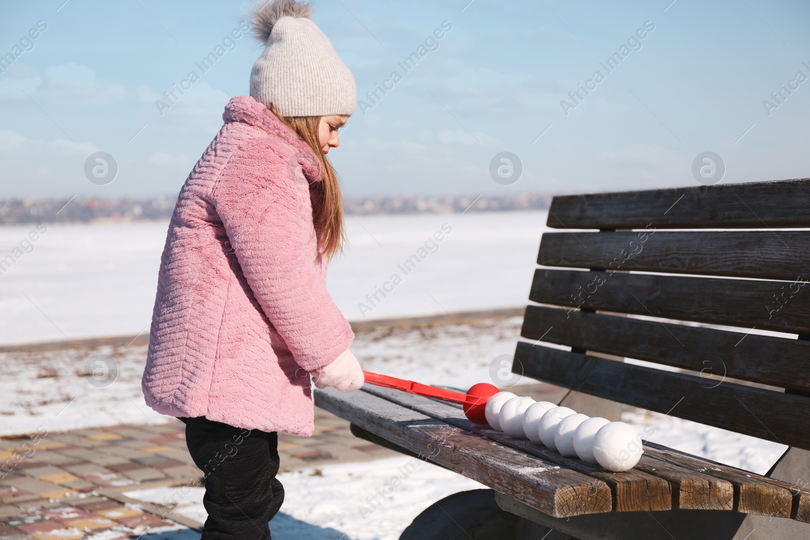 Photo of Cute little girl playing with snowball maker outdoors