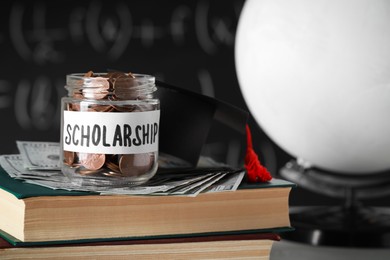 Photo of Scholarship concept. Glass jar with coins, graduation cap, dollar banknotes and books
