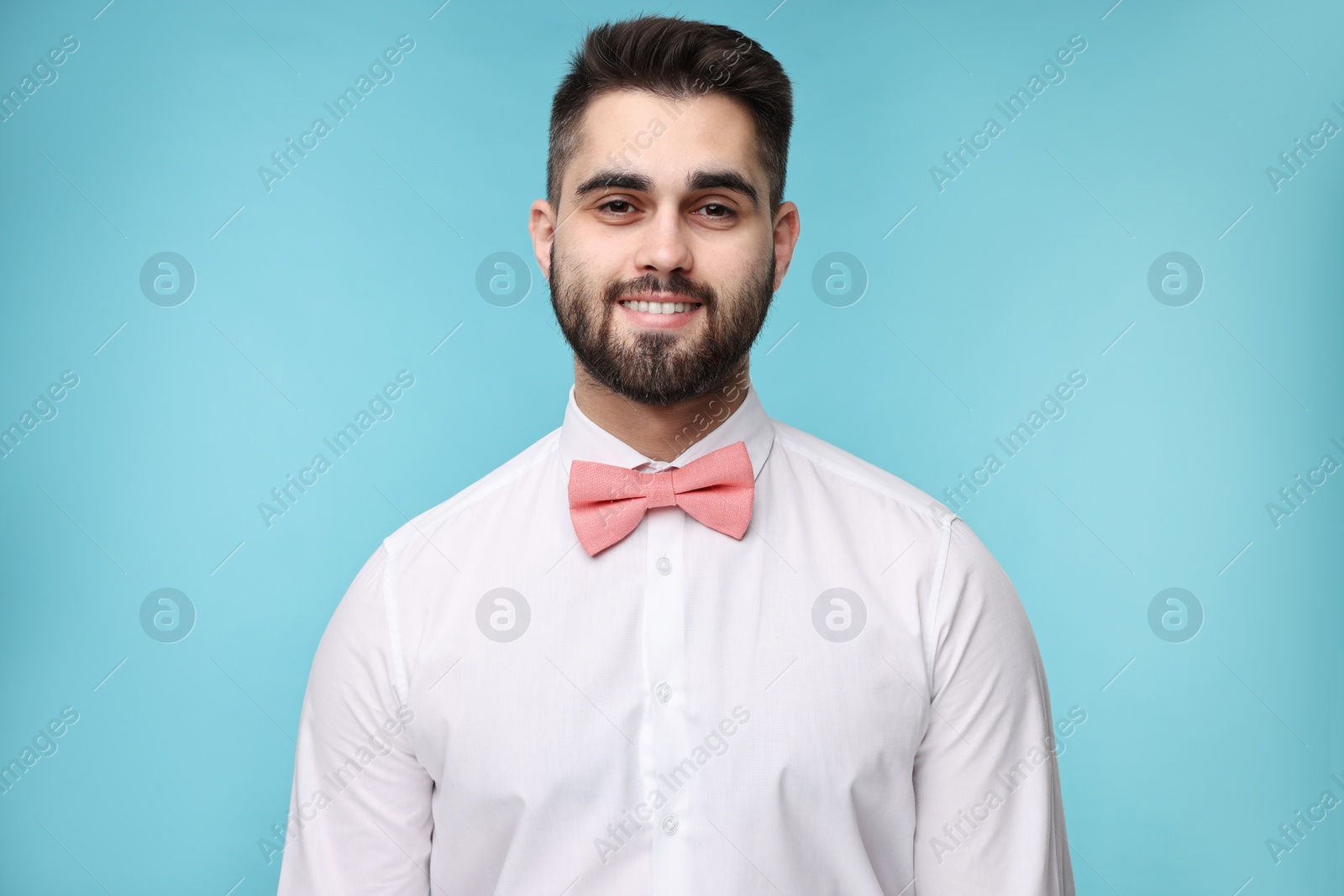 Photo of Portrait of smiling man in shirt and bow tie on light blue background