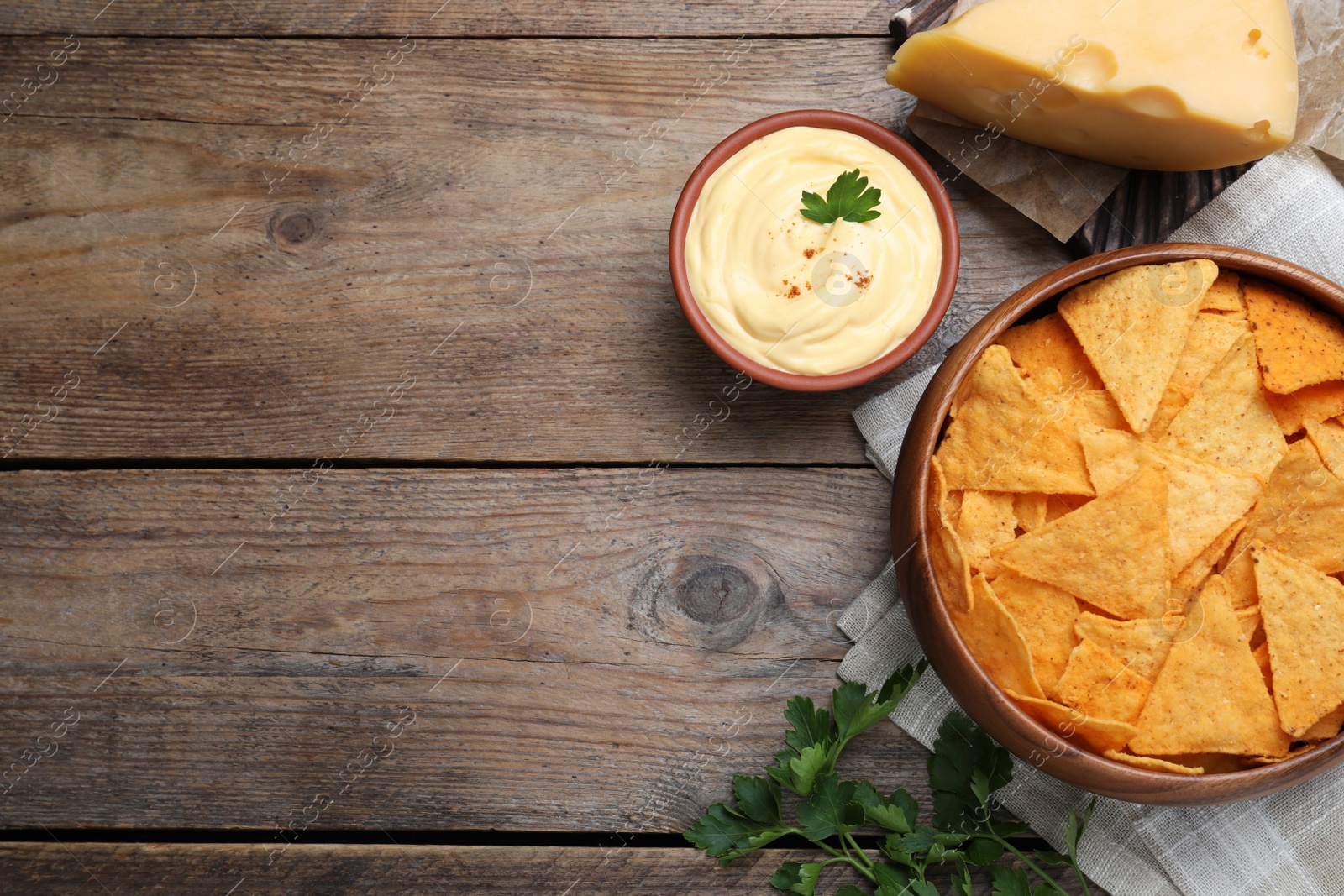 Photo of Delicious nachos and cheese sauce with parsley on wooden table, flat lay. Space for text