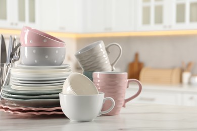 Many different clean dishware and cups on white marble table in kitchen. Space for text