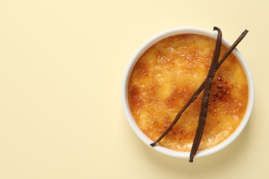 Delicious creme brulee with vanilla sticks on beige background, top view. Space for text