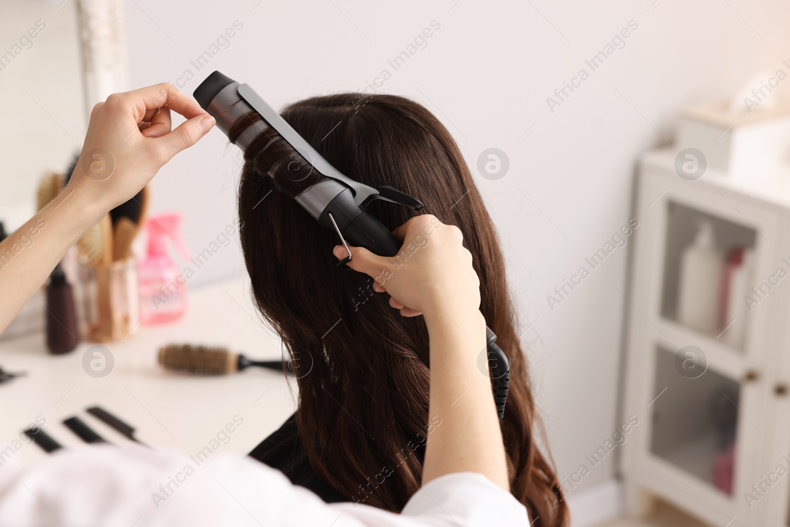 Photo of Hairdresser working with client using curling hair iron in salon, closeup