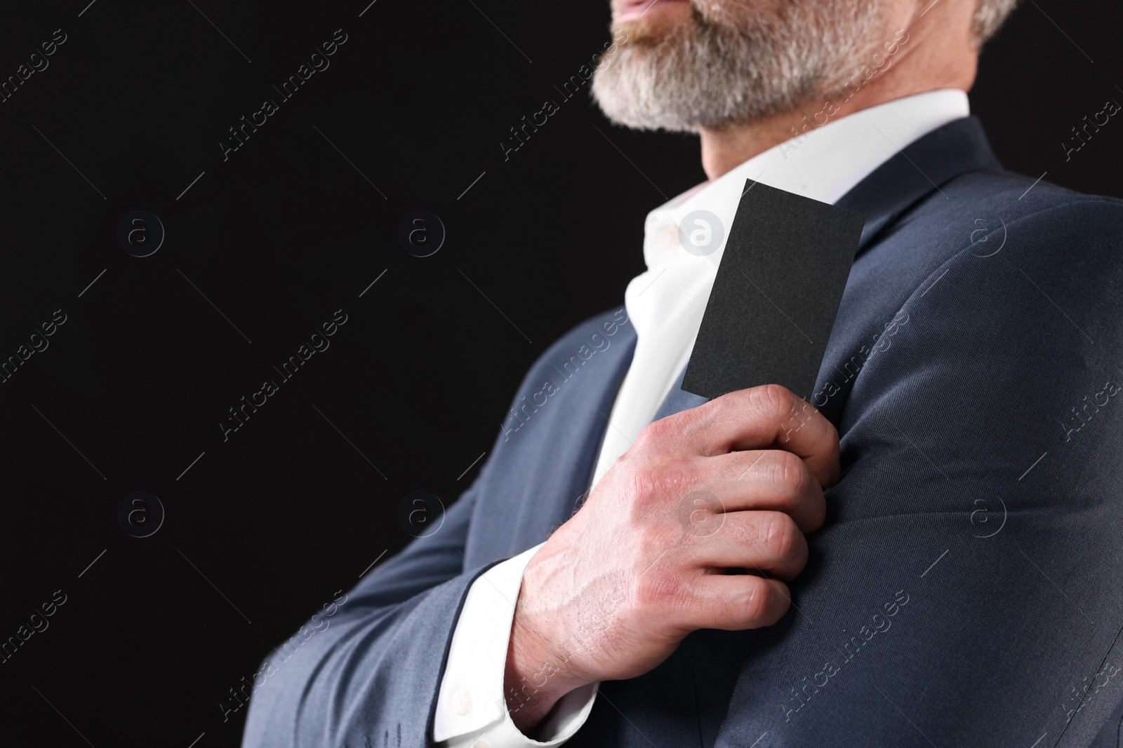 Photo of Businessman holding blank business card on black background, closeup. Space for text