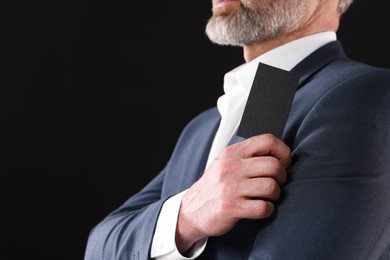 Businessman holding blank business card on black background, closeup. Space for text