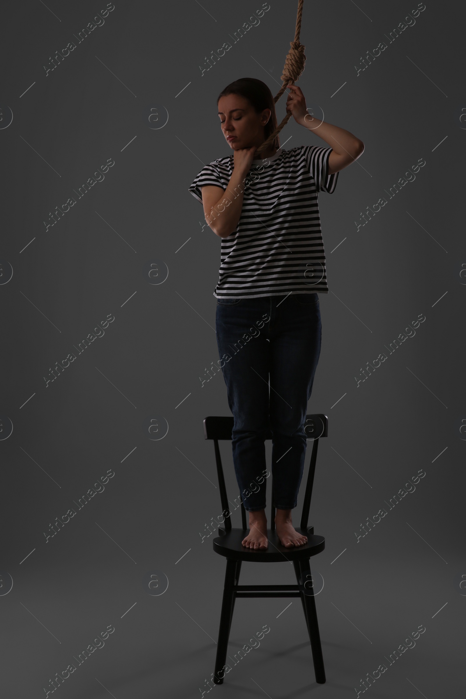 Photo of Depressed woman with rope noose standing on chair against grey background