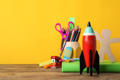 Photo of Bright toy rocket and school supplies on wooden desk. Space for text