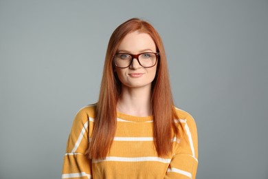 Portrait of young woman with gorgeous red hair and glasses on grey background