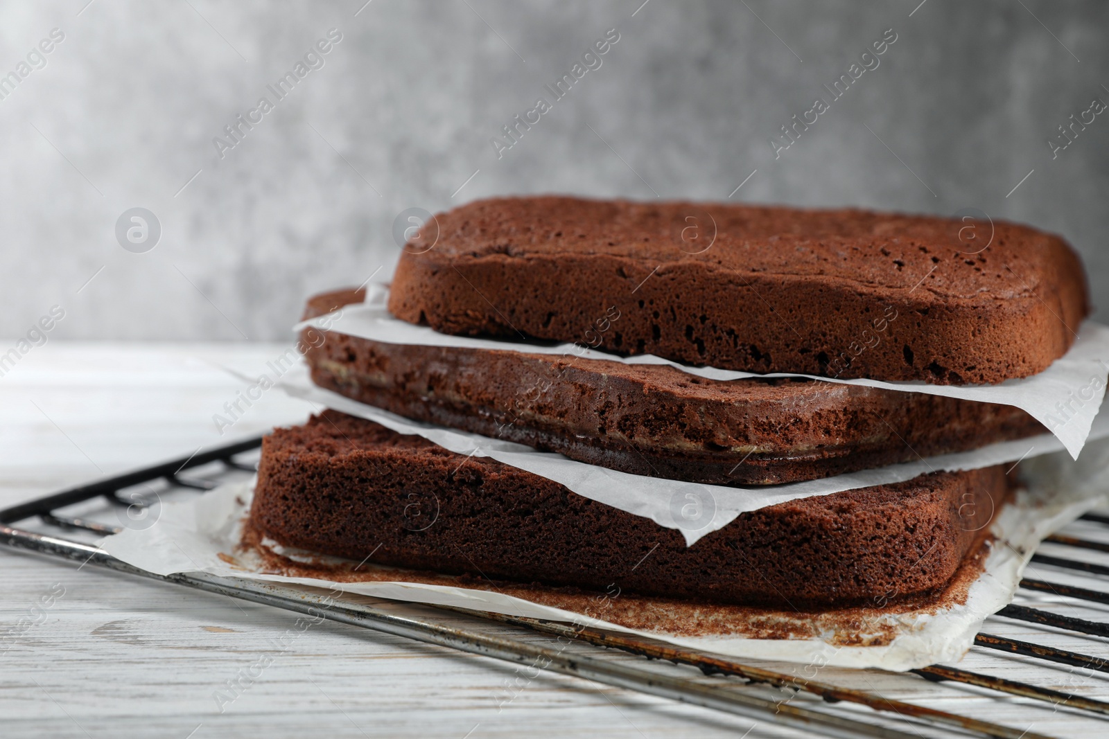 Photo of Layers of homemade chocolate sponge cake on white wooden table