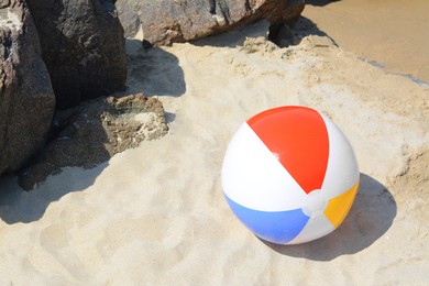 Colorful beach ball on sand near rocks, space for text