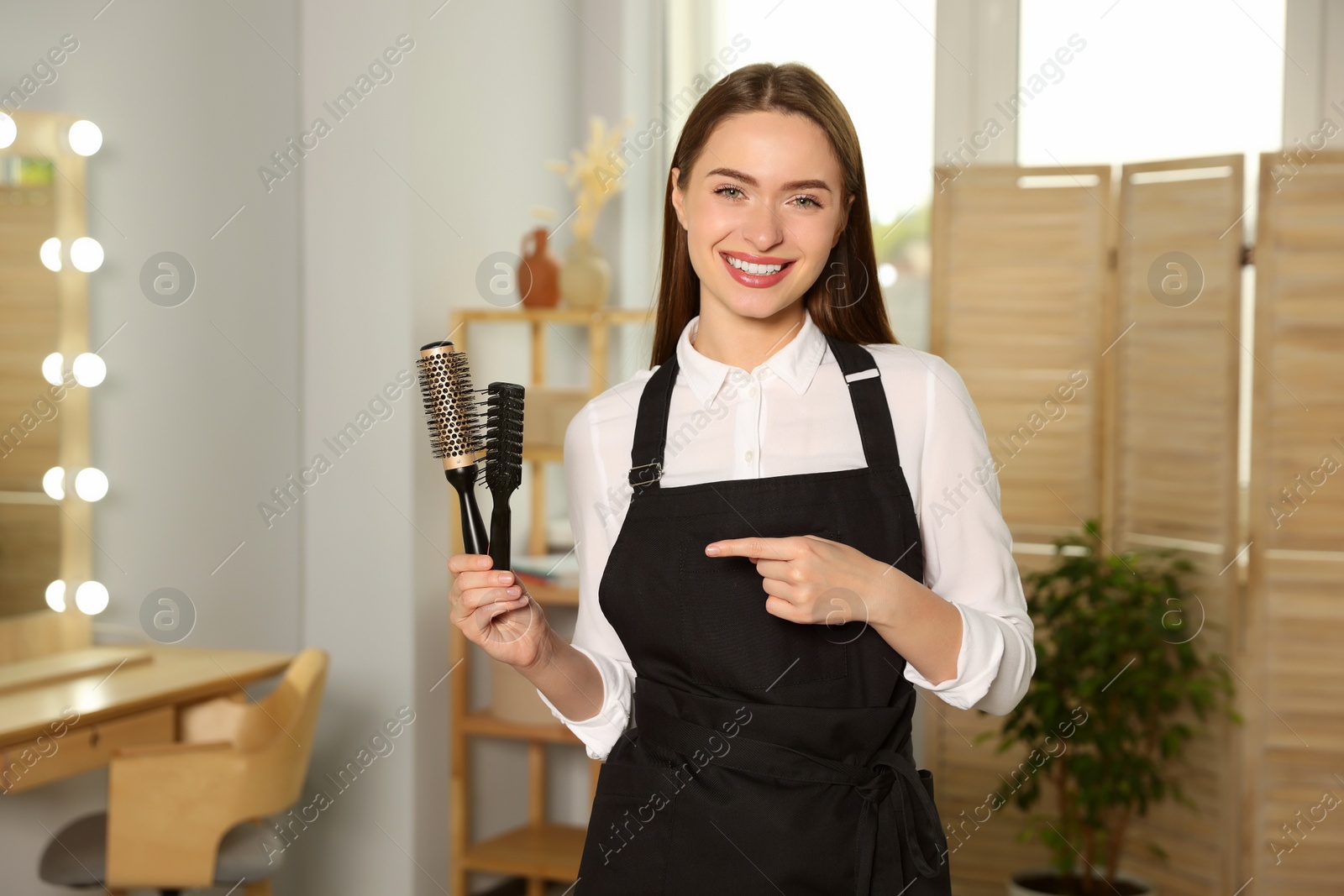 Photo of Portrait of happy hairdresser with brushes in beauty salon