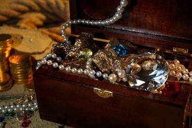 Photo of Chest with treasures, golden coins and scattered sand on floor, closeup