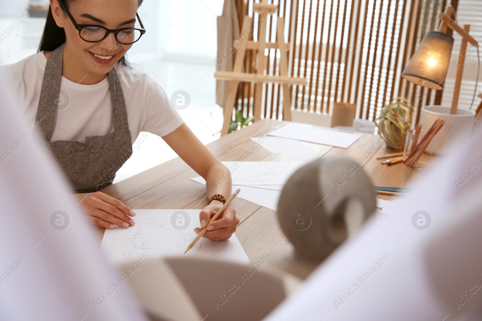 Photo of Young woman drawing male portrait at table indoors, closeup