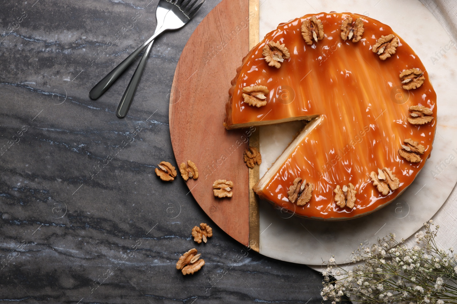 Photo of Delicious cheesecake with caramel and walnuts on black marble table, flat lay. Space for text