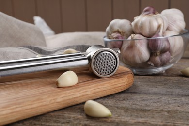 Garlic press and cloves on wooden table, closeup