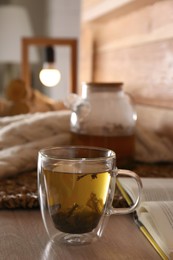 Photo of Freshly brewed tea and open book on wooden table in room. Cozy home atmosphere