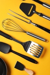 Photo of Different spatulas and other kitchen utensils on orange background, flat lay