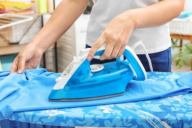 Woman ironing clothes on board indoors, closeup