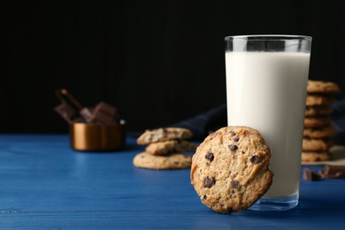 Tasty chocolate chip cookies and glass of milk on blue wooden table. Space for text