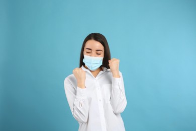 Emotional woman with protective mask on light blue background. Strong immunity concept