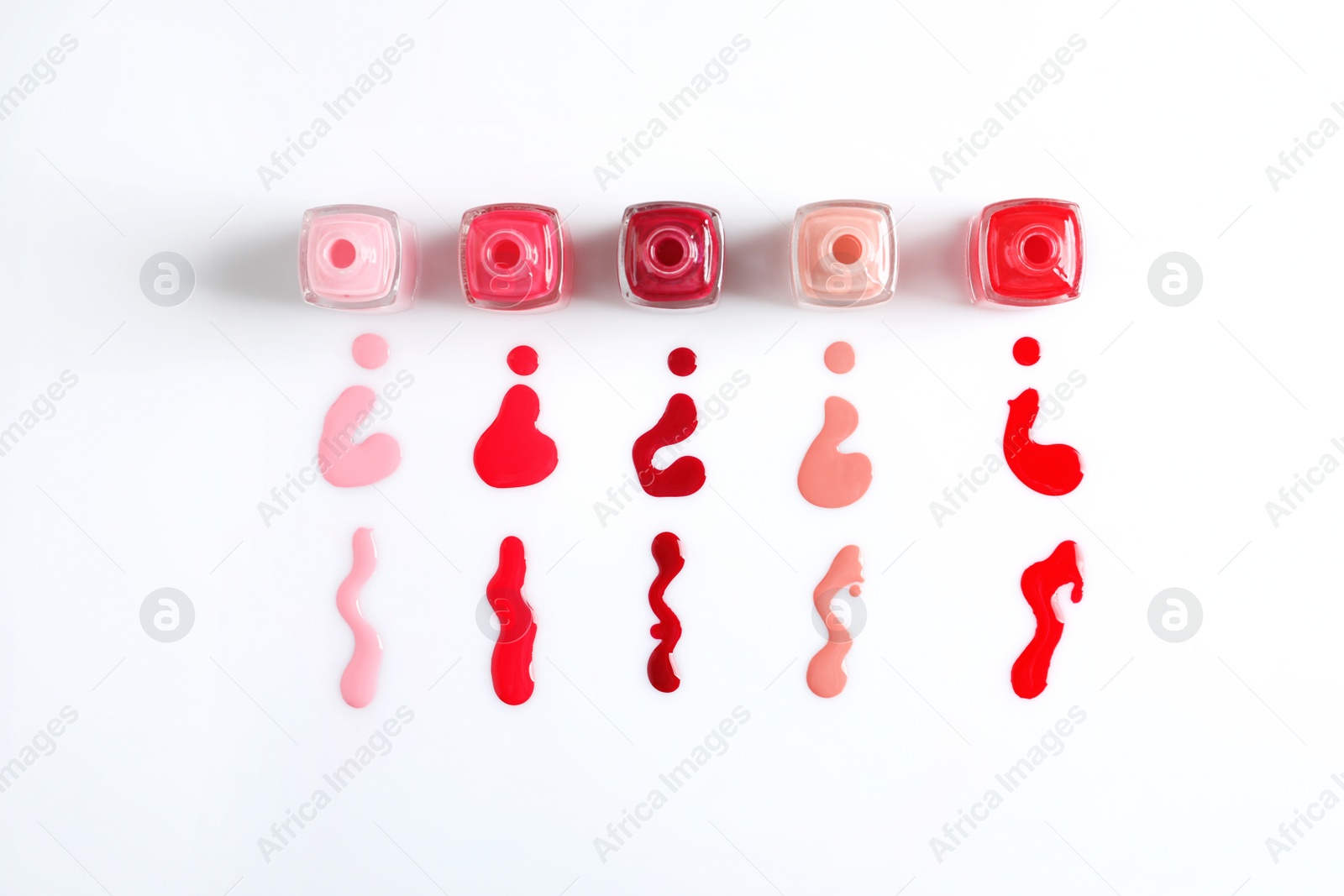 Photo of Spilled colorful nail polishes and bottles on white background, top view