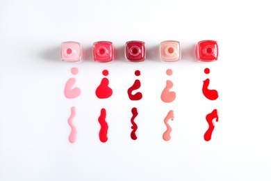 Spilled colorful nail polishes and bottles on white background, top view