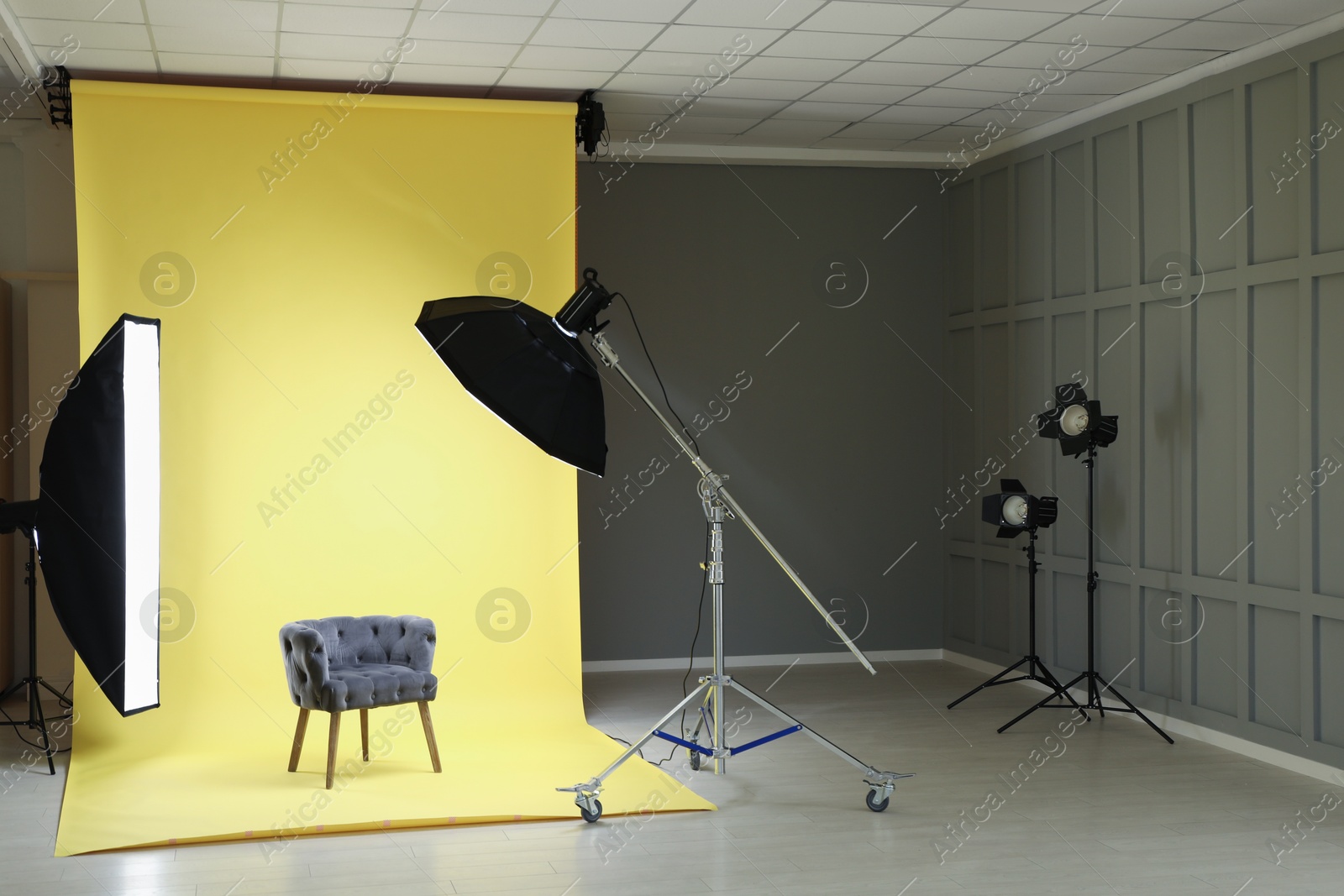 Photo of Yellow photo background, armchair and professional lighting equipment in modern studio