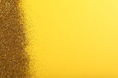 Photo of Shiny golden glitter on yellow background, top view. Space for text