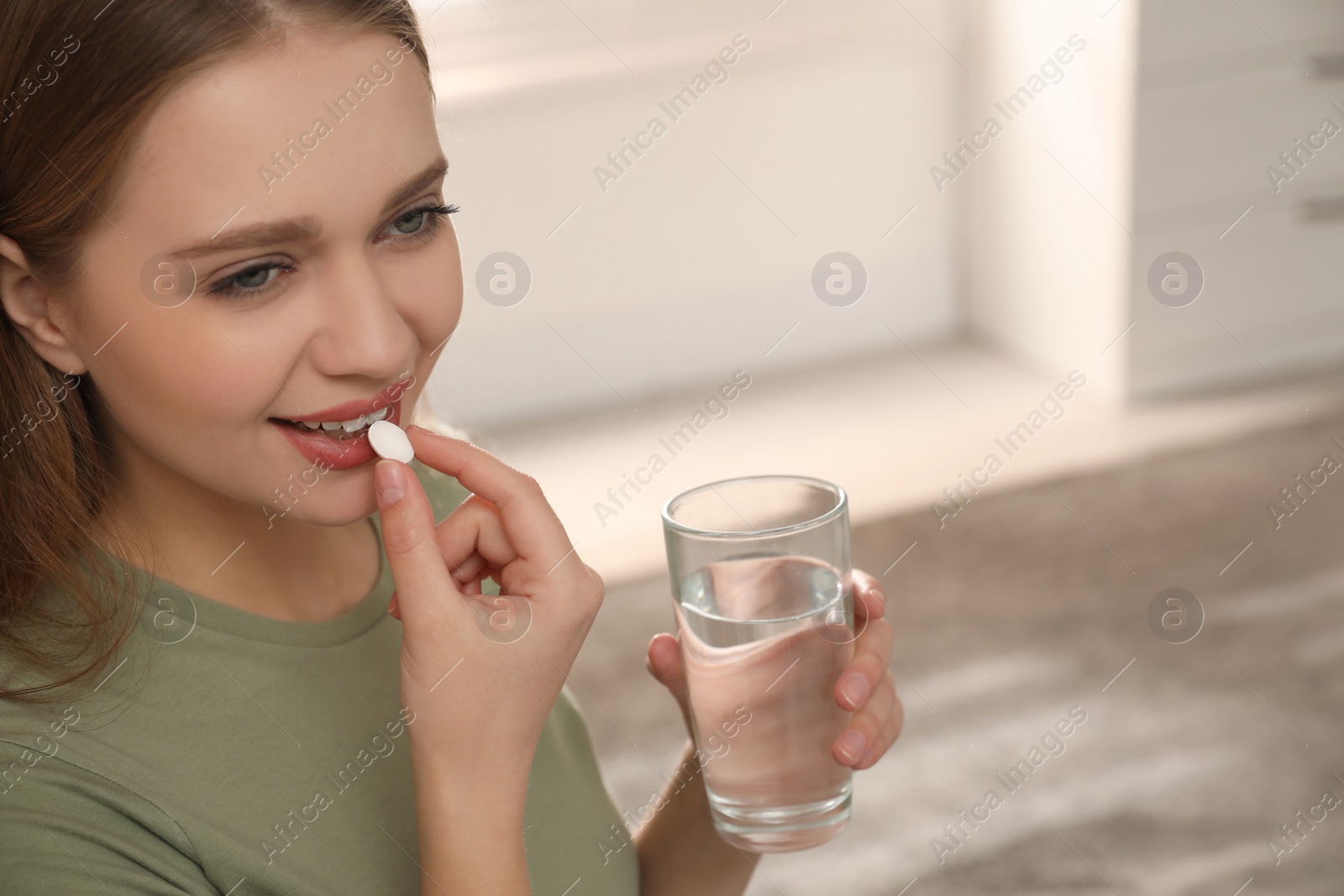 Photo of Young woman with glass of water taking vitamin pill at home