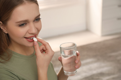 Photo of Young woman with glass of water taking vitamin pill at home
