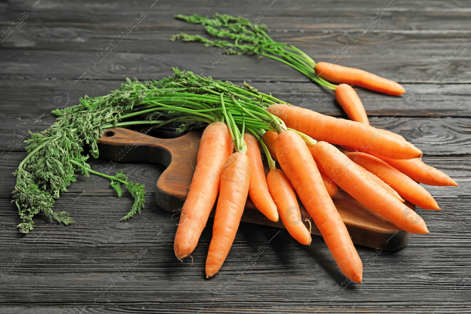 Photo of Board with ripe carrots on wooden background