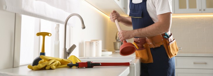 Plumber with plunger near clogged sink in kitchen, closeup. Banner design