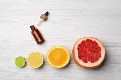 Photo of Bottle of citrus essential oil and fresh fruits on white wooden table, flat lay. Space for text
